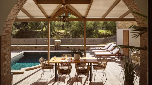 A covered outdoor seating area with a pool, wicker chairs, and a table with drinks.