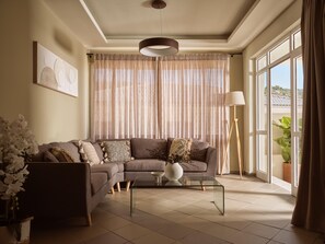 Un salón con un sofá modular, una mesa de centro de cristal, una lámpara de pie y un ventanal con cortinas.