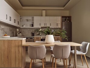 Una cocina moderna con armarios blancos, encimera de mármol y comedor con mesa de madera y cuatro sillas.