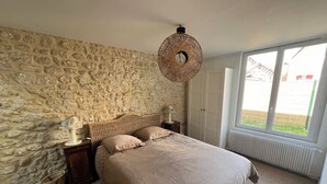 Ein Schlafzimmer mit Steinsandsteinwand, einem Bett mit gewebtem Kopfteil, einer Nachttischlampe und einem großen Fenster mit Blick ins Freie.