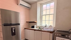 Eine kleine Küche mit einem Edelstahlkühlschrank, einer Spüle mit Geschirabrücke, einem Herd und einem Fenster für natürliches Licht.