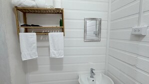 Ein Badezimmer mit einem Holzbodenregal, das Handtücher und Pflegeprodukte beherbergt, einem kleinen Spiegel und einem weißen Waschbecken.