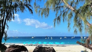 Ein Strand mit klarem, blauem Wasser, Booten und Sonnenschirmen.