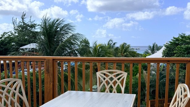 Eine Holzterrasse mit Tisch und Stühlen, mit Blick auf einen Strand und Palmen.