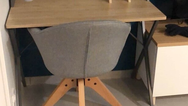 Ein Zimmer mit einem Holztisch, einem grauen Stuhl und einem weißen Schreibtisch.