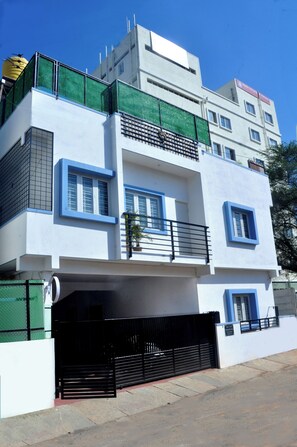 A modern multi-story building with a flat roof, balconies, and a gated entrance. - Spacious 7-bedroom villa in Bengaluru with AC (Bengaluru)