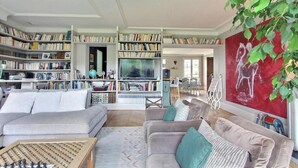 A spacious living room with a large bookshelf, two sofas, a coffee table, and a TV. - A PERFECT BLEND OF COMFORT, ELEGANCE & TRANQUILLITY AT BLVD SAINT GERMAIN (Paris)