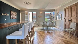 Un'ampia stanza con pavimento in legno a spina di pesce, un'area pranzo con tavolo e sedie, e vista del balcone esterno.