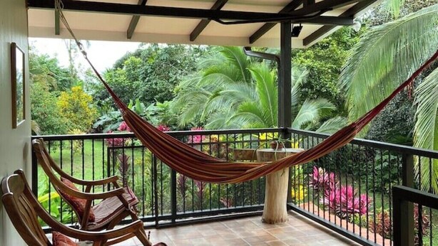 A balcony with a hammock and wooden chairs, surrounded by lush greenery and a tiled floor. - Full lodging, lookout point  (Mirador)