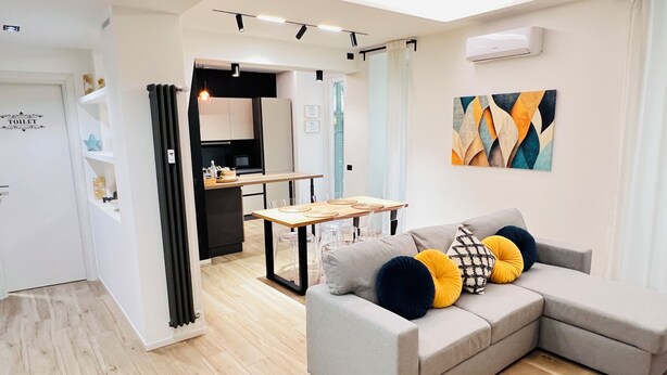 A modern living room with a grey sofa, a dining table, and a kitchen in the background. - House Of Victories (Roma)