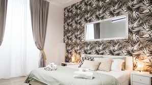 A modern bedroom with a large bed, a nightstand, a bedside table with a lamp, and a wall-mounted mirror. - House Of Victories (Roma)