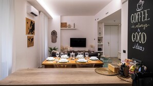 A dining area with a wooden table set for six, a flat-screen TV, and a blackboard with a coffee quote. - House Of Victories (Roma)