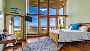 A bedroom with a bed, a desk, a chair, a TV, and a view of the ocean. - Villa Seamone | Beachfront, Pet Friendly (Galveston)