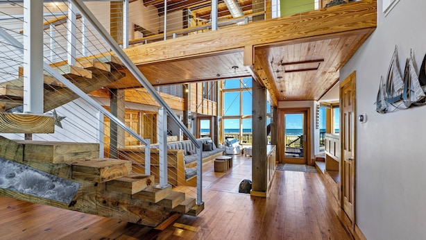 A spacious interior with a wooden staircase, high ceilings, and large windows offering views. - Villa Seamone | Beachfront, Pet Friendly (Galveston)