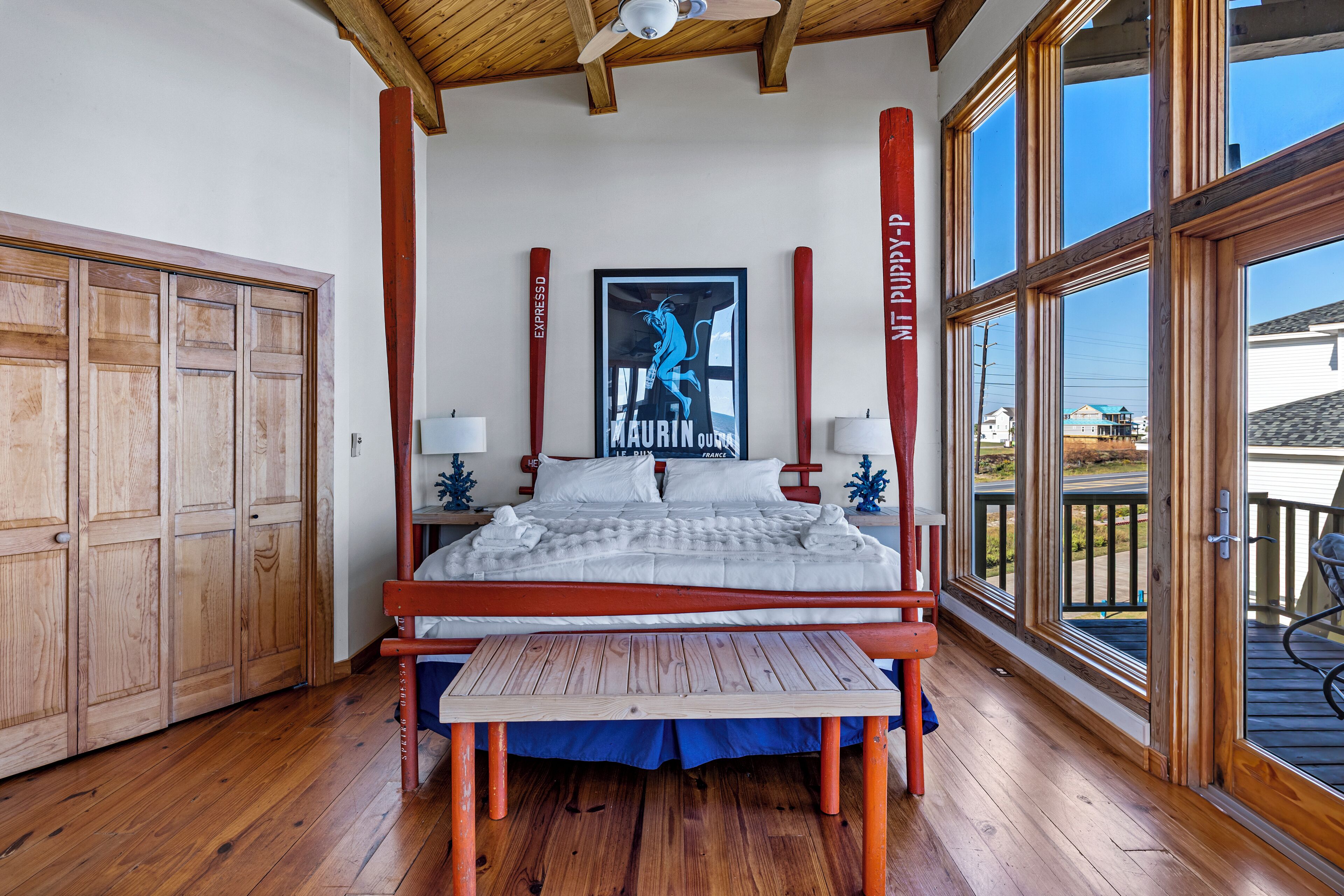 Ein Schlafzimmer mit einem Himmelbett, Holzboden, Deckenventilator und großen Fenstern.
