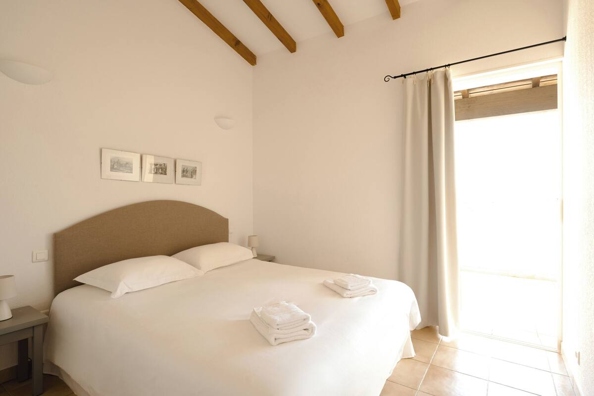 A bedroom with a bed, a nightstand, a lamp, and a window with curtains.