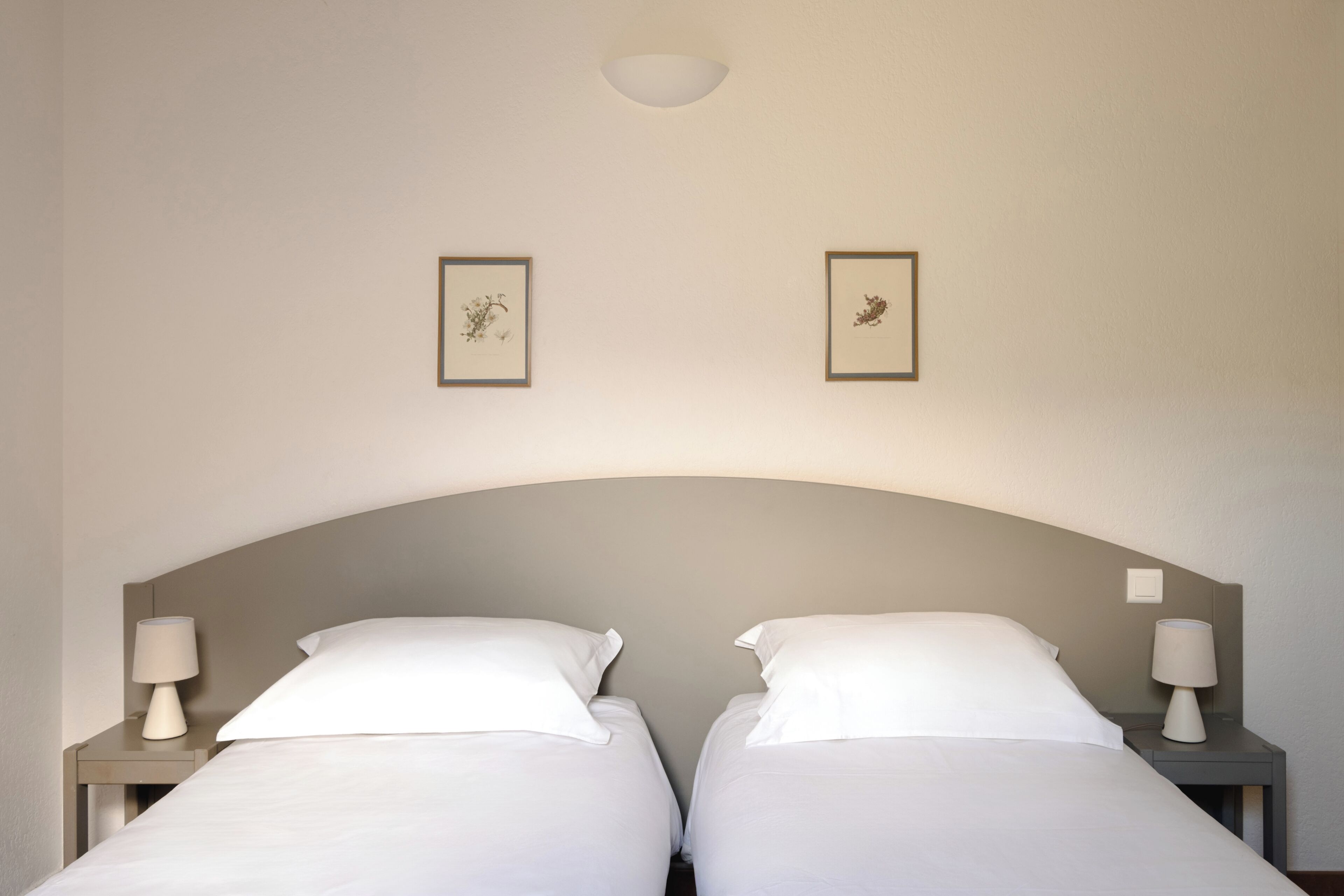 A double bed with a curved headboard, two bedside tables with lamps, and two framed pictures on the wall.