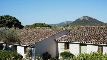 A traditional building with a tiled roof, surrounded by greenery and a mountain in the background.