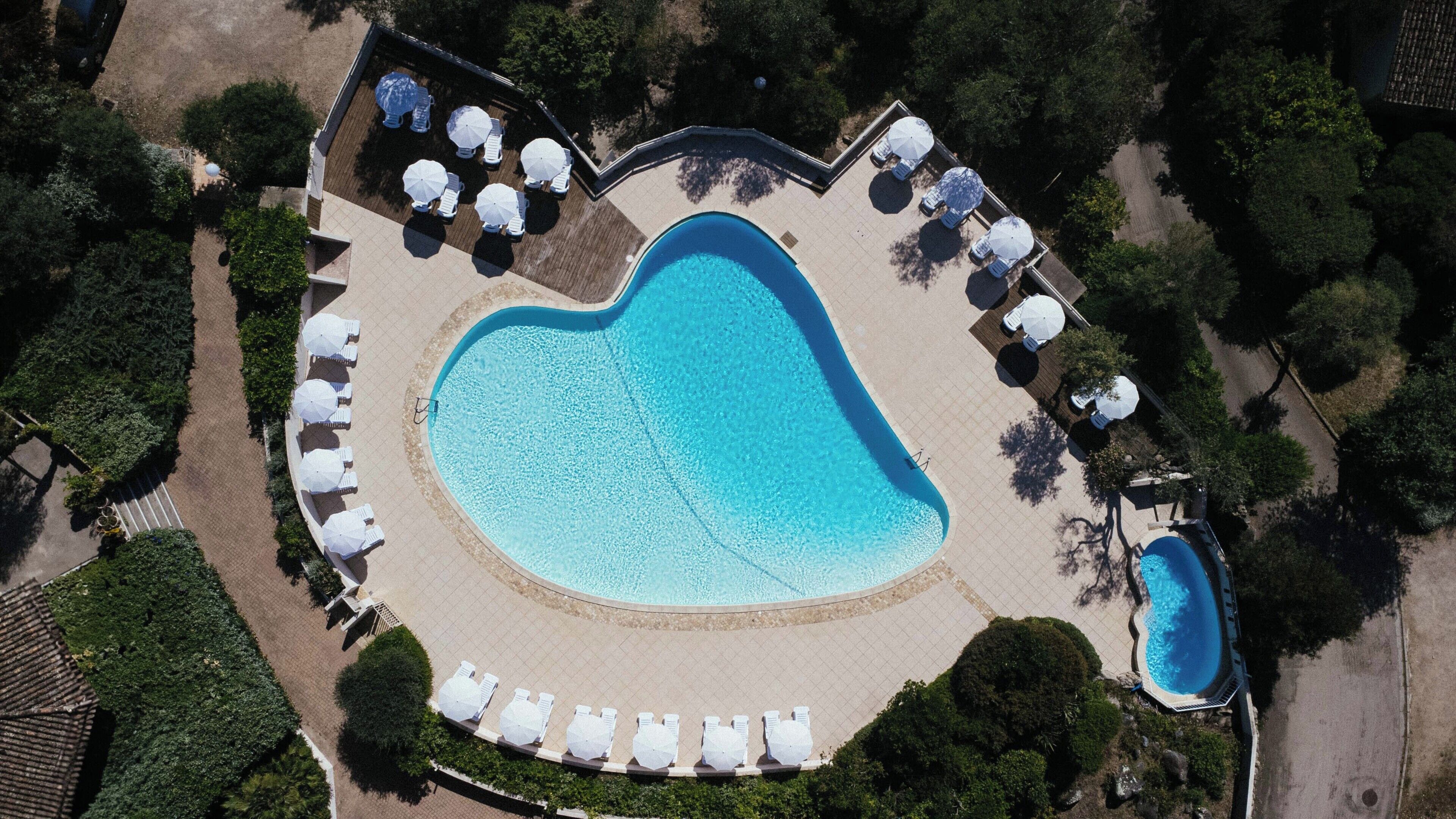 An aerial view of a heart-shaped swimming pool surrounded by lounge chairs and umbrellas.