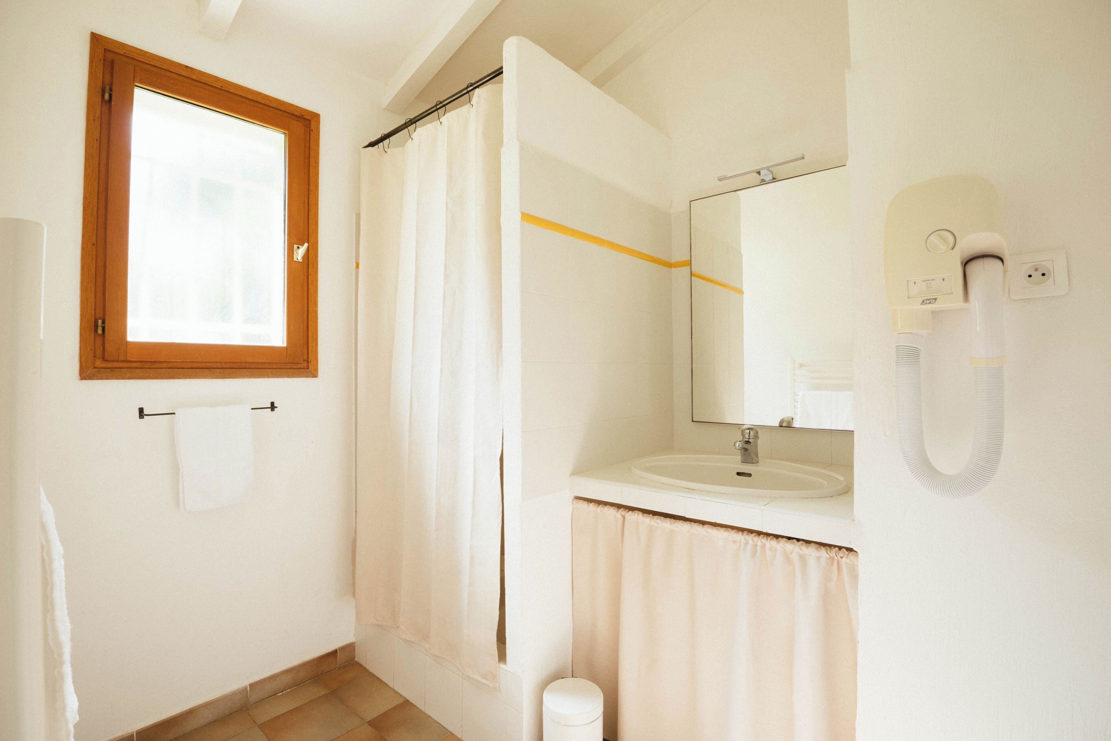 A bathroom with a wooden-framed window, a white sink, a mirror, and a shower curtain.