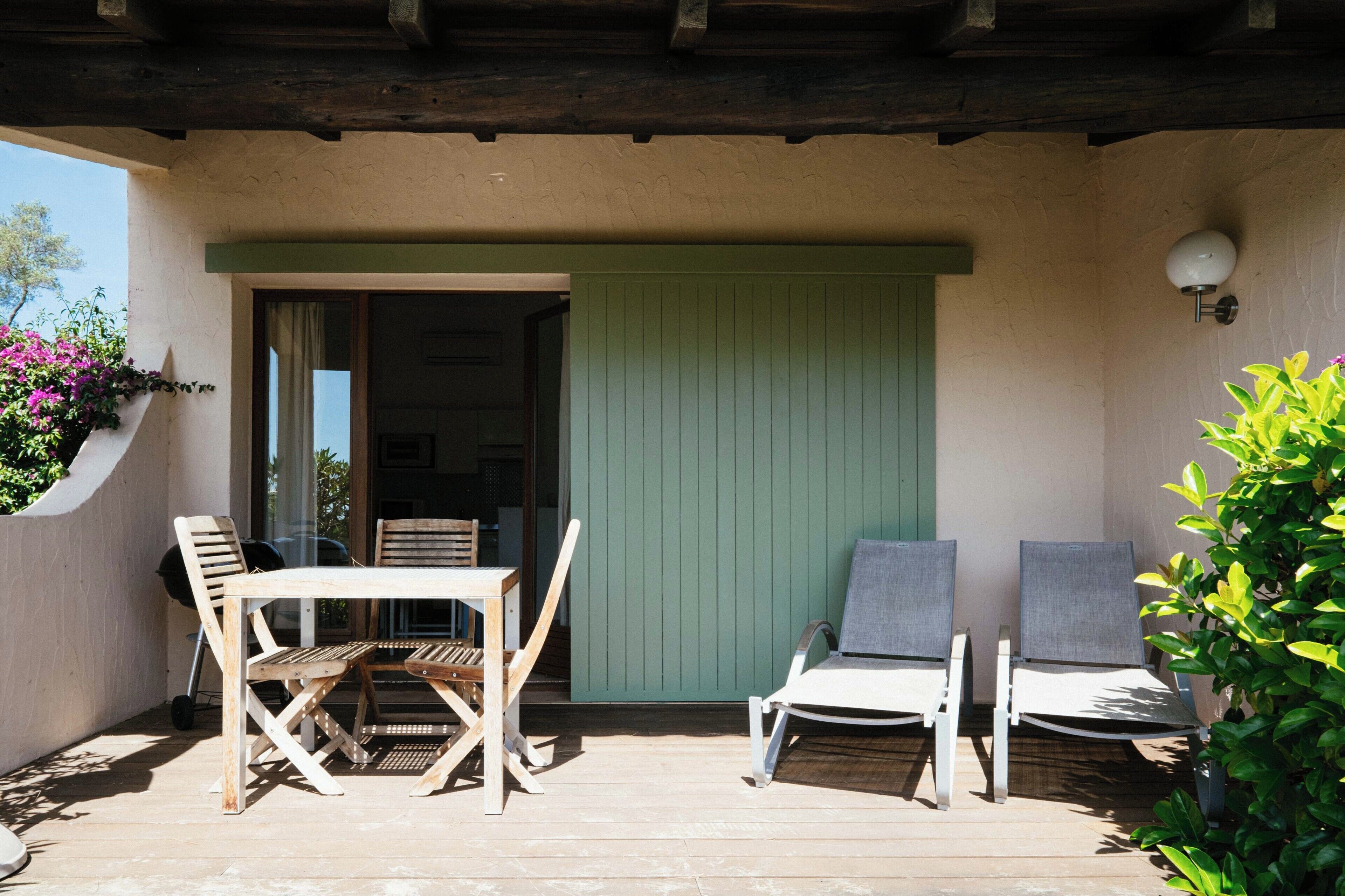 An outdoor patio with a table and chairs, a sliding door, and a wall-mounted light fixture.