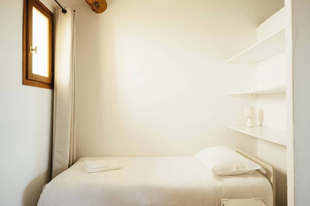 A single bed with a wooden headboard, a bedside table with a lamp, and a window with curtains.