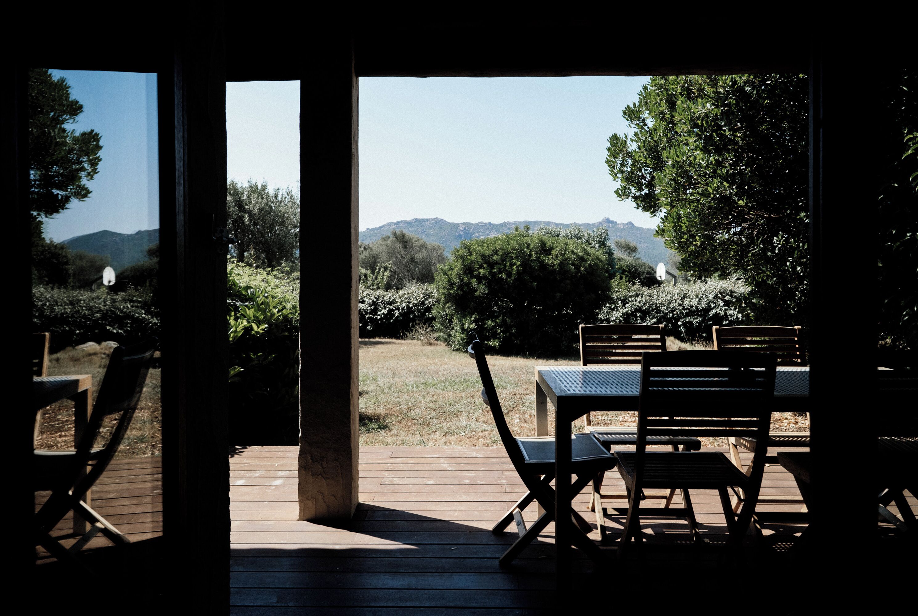 An outdoor patio with a table and chairs, a wooden deck, and a view of a hilly landscape.