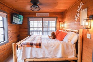 A wooden cabin bedroom with a bed, pillows, a blanket, a TV mounted on the wall, and a window. - Video-game themed arcade! Spacious 3 br cabin! (Sevierville)