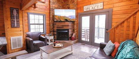 A cozy log cabin interior with a fireplace, leather furniture, and a welcome sign.