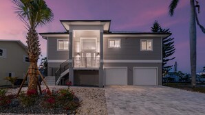 Ein zweistöckiges Haus mit überdachter Garage, einer Treppe und einem angelegten Vorgarten mit einer Palme und Zierpflanzen.