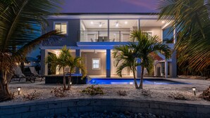 Ein modernes, zweistöckiges Haus mit Schwimmbad, Palmen und einer Terrasse.