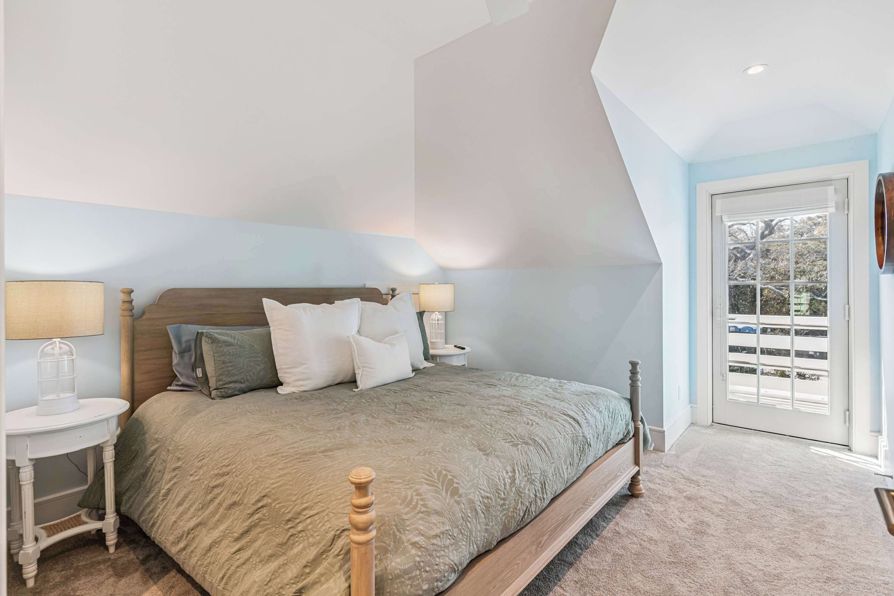 A bedroom with a bed, two bedside tables, a lamp, and a door leading to an outdoor area.