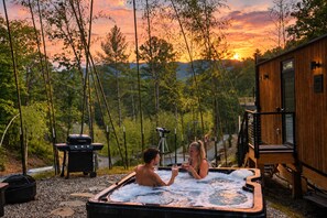 Un bain à remous où se trouvent deux personnes, entouré d’arbres et d’une construction en bois.