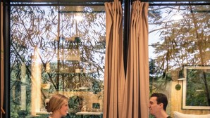 Deux personnes sont assises à une table dans une pièce moderne, dotée d’un plancher en bois et de grandes fenêtres.