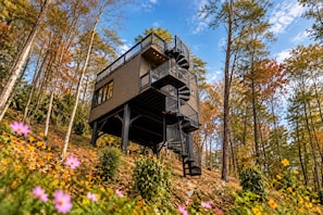 A treehouse with a spiral staircase, surrounded by autumn foliage and flowers. - Stargazing Treehouse - Rooftop Hot Tub 35 feet in the air! (Sevierville)