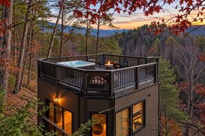 A two-story cabin with a hot tub on the upper deck, surrounded by a forest. - Brand New Stargazing Treehouse - Hot Tub - Fire Pit (Sevierville)