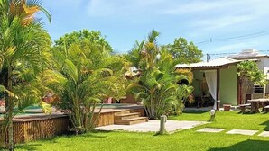 Ein gepflegter Garten mit einer Holzdielen-Terrasse, Palmen und einem kleinen Gebäude mit einem Ziegeldach.