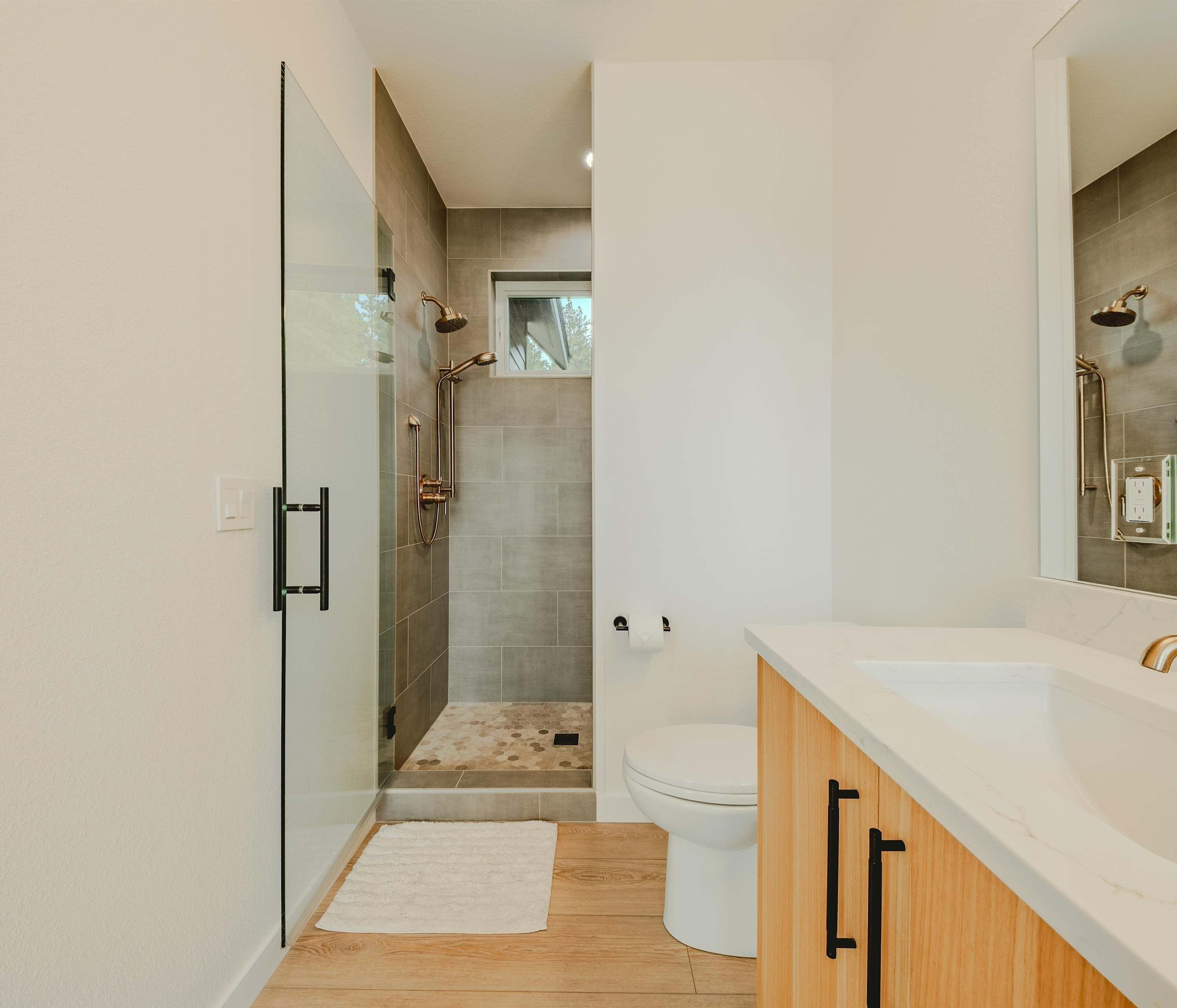 A modern bathroom with a glass shower enclosure, a white toilet, and a wooden vanity with a white countertop.