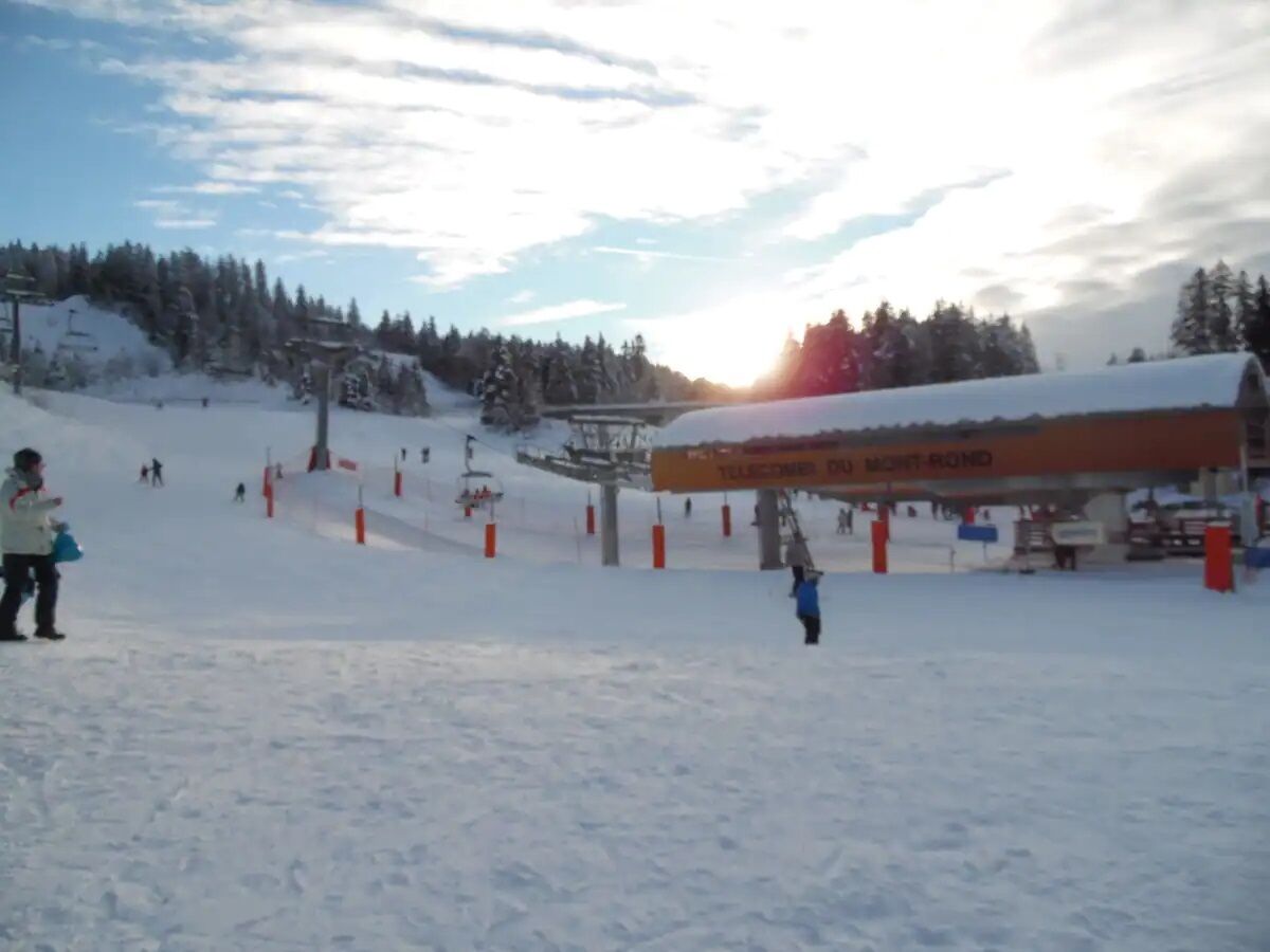 Pista da sci innevata con una seggiovia e un edificio con la scritta "TELCOMBER B. MONT. ROND".