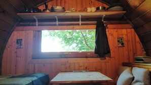 A cabin interior with a wooden interior, a window with a view of trees, a table, and a bed. - Col de la Faucille Tonneau (Mijoux)