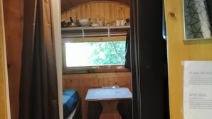 A compact cabin with a kitchenette, a small dining table, and a window overlooking greenery. - Col de la Faucille Tonneau (Mijoux)
