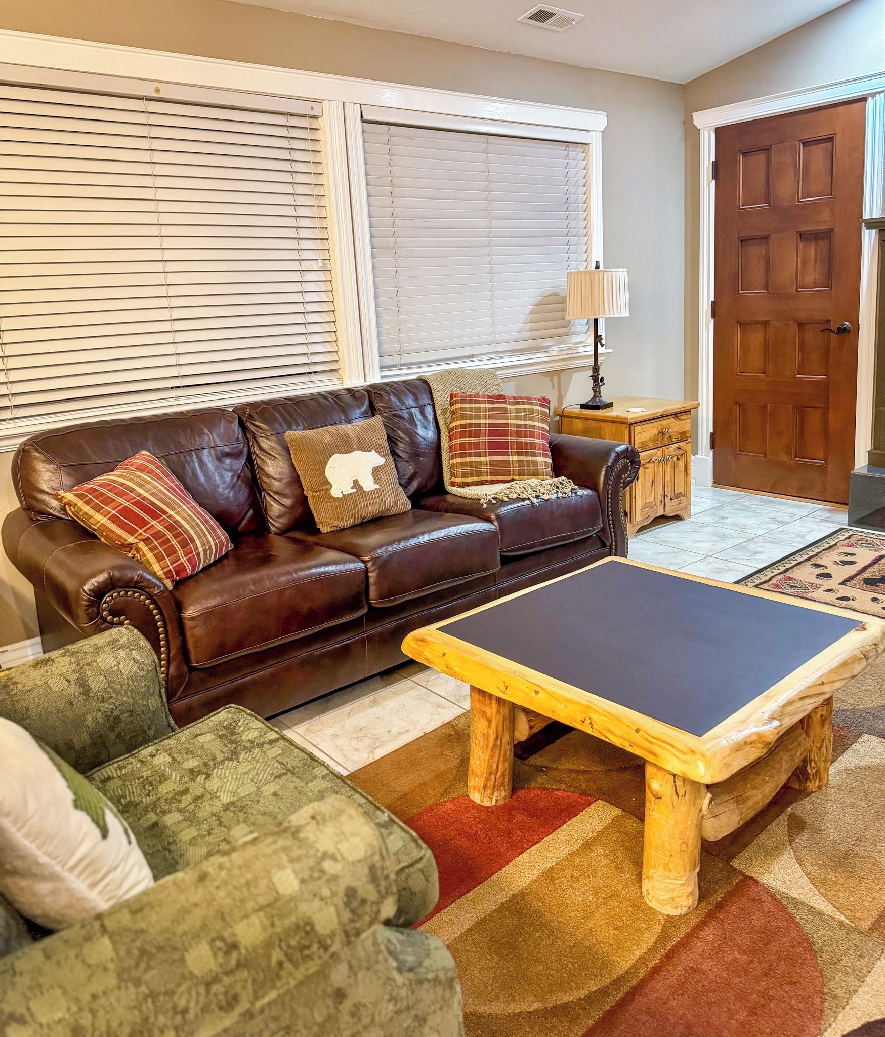 A living room with a brown leather sofa, a wooden coffee table, and patterned rugs.