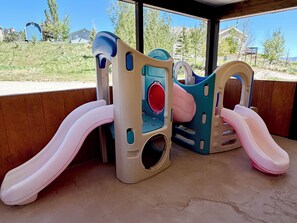 Een speelconstructie voor kinderen met glijbanen en klimmogelijkheden, met op de achtergrond een woonwijk.