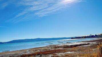 A clear sky over a lake with distant mountains and a flat, grassy shoreline.