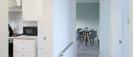A modern kitchen with white cabinets, a microwave, and a stove. There is a dining area with a round table and chairs.