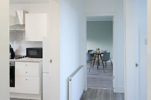 A modern kitchen with white cabinets, a microwave, and a stove. There is a dining area with a round table and chairs. - Harbour View in Troon (South Ayrshire)