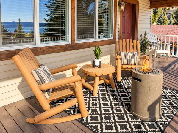 Une terrasse en bois avec un fauteuil à bascule, une petite table avec une plante et un foyer.