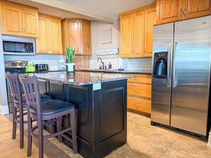 Una cocina con armarios de madera, un refrigerador de acero inoxidable, un microondas, una cafetera y una planta en maceta.