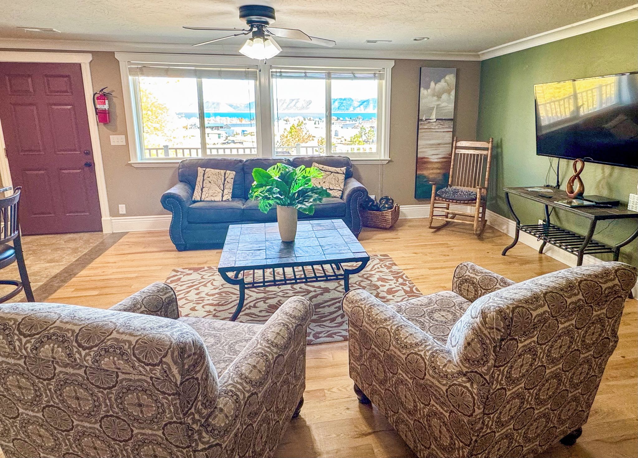 A living room with a sofa, patterned armchairs, a coffee table, a television, and a painting.