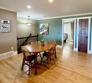A dining room with a wooden table and chairs, a painting on the wall, and a staircase leading to another room.